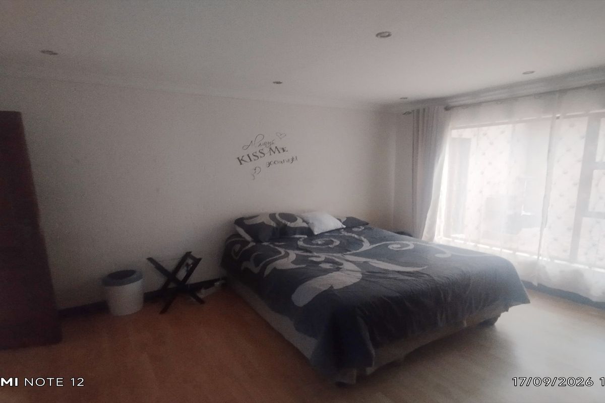 A spacious bedroom featuring laminate flooring, recessed downlighting, and a large window allowing for natural light.