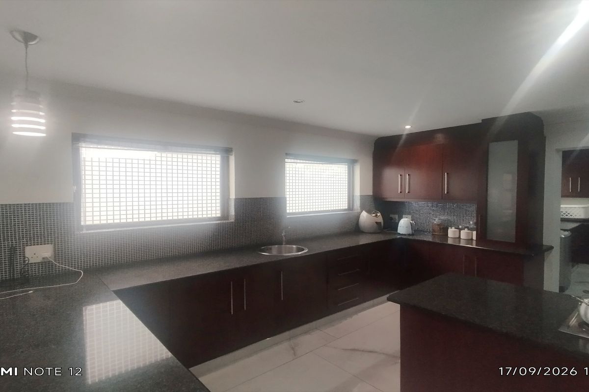 A functional kitchen featuring dark wood cabinetry, granite countertops, mosaic tile backsplash, and tiled flooring with an adjacent scullery area.