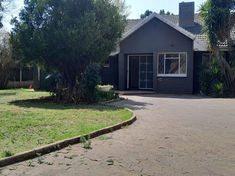 Front view of a single-story house featuring a brick driveway, tiled roof, and established garden area.