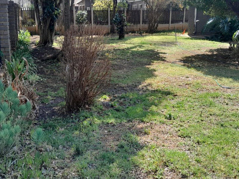A private rear garden area featuring established trees, patchy lawn, and secure brick and metal perimeter fencing.