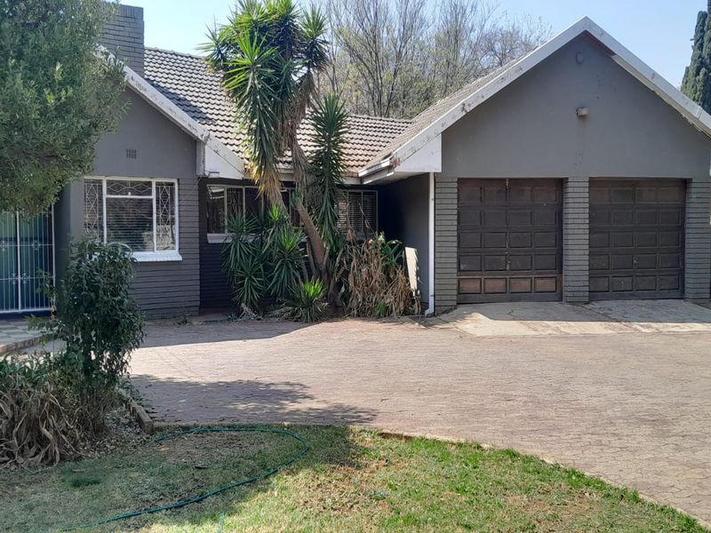 Front elevation of a house featuring a double garage, brick paved driveway, and tiled roof, set within a mature garden.