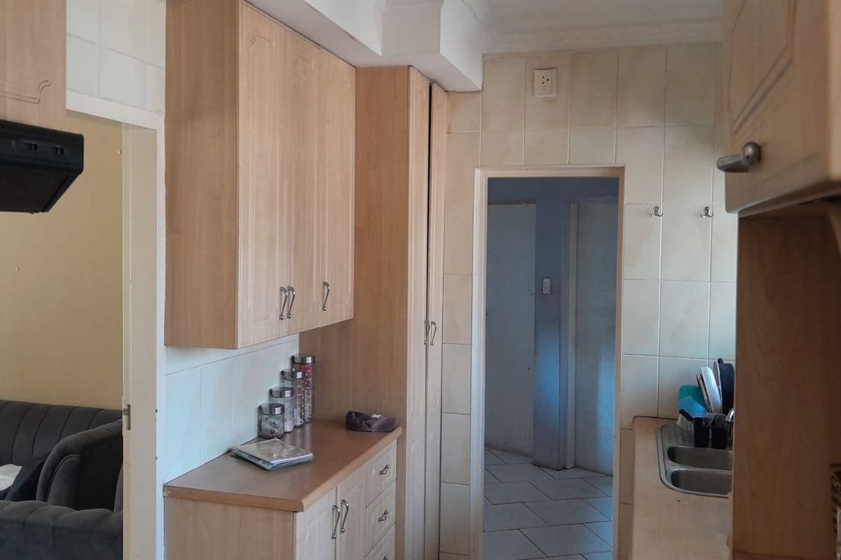 A functional kitchen area featuring light wood-tone cabinetry, laminate countertops, a double bowl sink, and tiled splashbacks with an integrated extractor fan.
