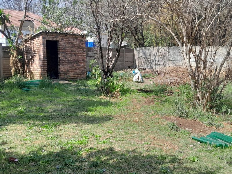 A spacious backyard featuring a brick outbuilding and precast concrete boundary walls, currently requiring significant landscaping and maintenance to improve its overall appeal.