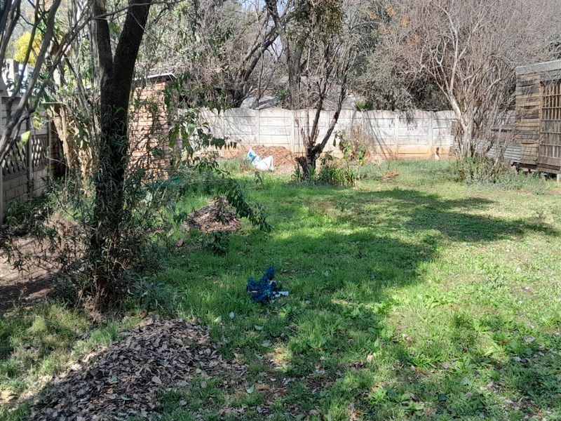 A spacious backyard garden featuring a precast concrete boundary wall and a wooden storage shed, requiring landscaping and maintenance to improve its overall appeal.