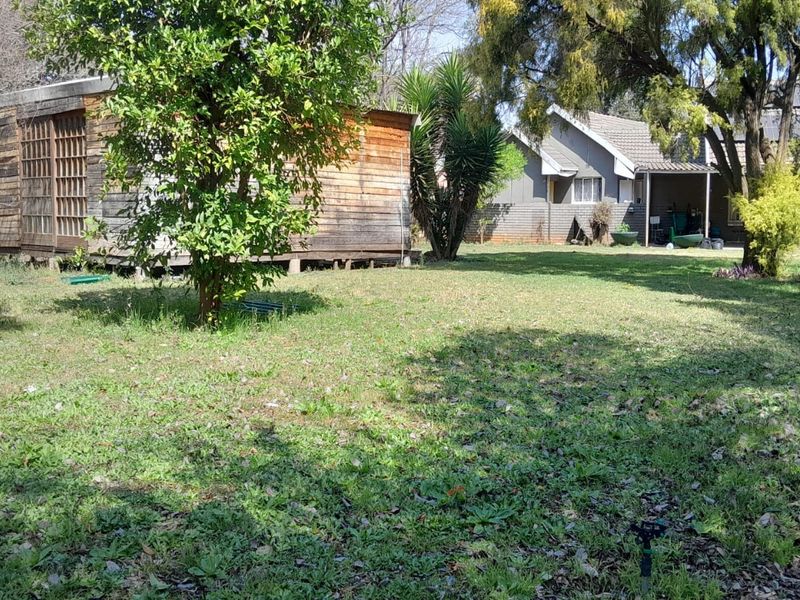 Spacious rear garden featuring a mature lawn, established trees, and a detached wooden outbuilding structure.