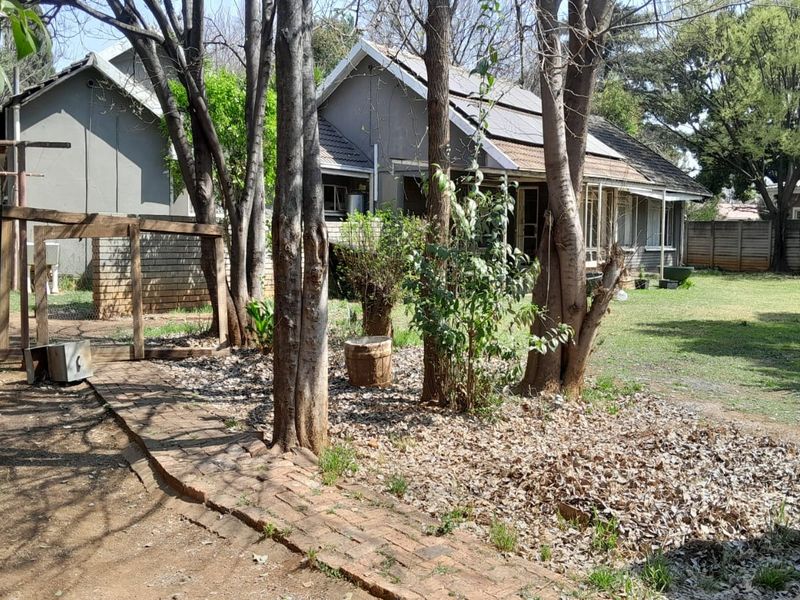 Rear view of the house featuring a large garden, brick pathway, and solar panels installed on the tiled roof.