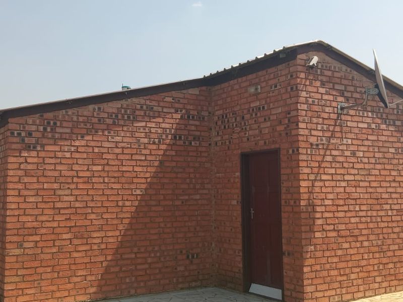 A view of the front exterior of a face brick house featuring a corrugated metal roof and a paved walkway.