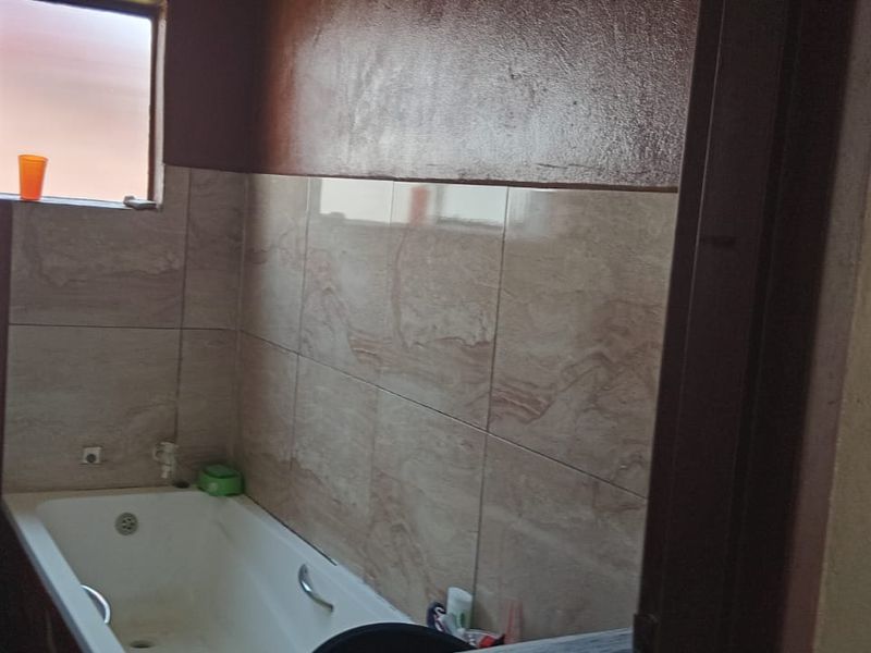 A functional bathroom featuring a bathtub, toilet, and tiled splashback, currently requiring cosmetic updates and finishing of wall surfaces.