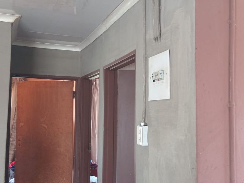 A hallway area featuring unfinished plaster walls, exposed electrical conduit, and standard internal door frames, requiring cosmetic finishing and maintenance.