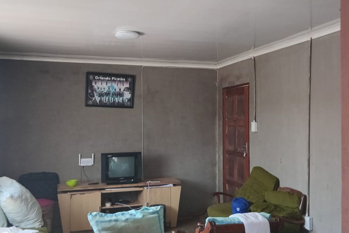 A living room featuring unfinished grey walls, surface-mounted electrical conduit, and a timber door, requiring cosmetic updates to improve the overall finish.