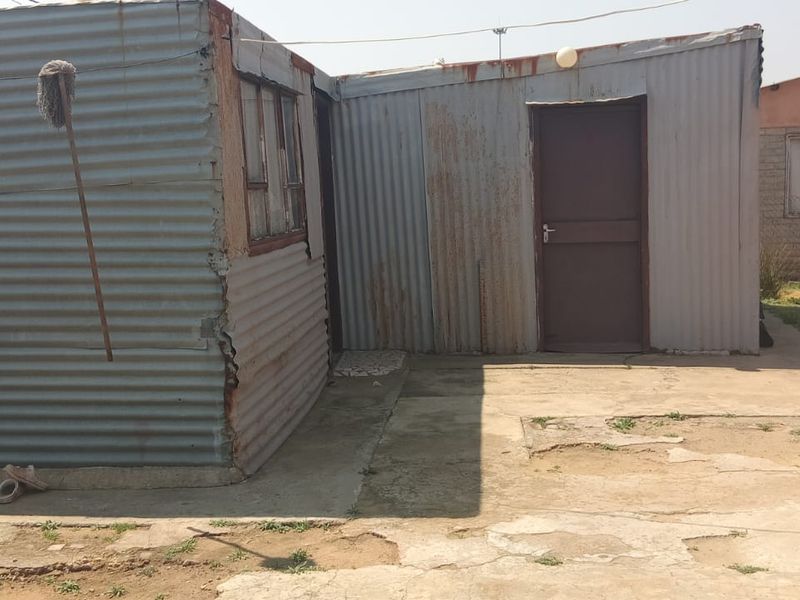 Rear exterior view of the property featuring corrugated iron structures and a concrete paved yard area showing signs of wear.