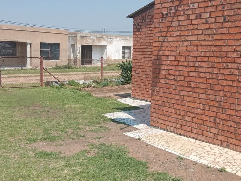 A view of the rear exterior featuring exposed brick wall construction, a crazy paving walkway, and a grassed yard area enclosed by wire fencing.