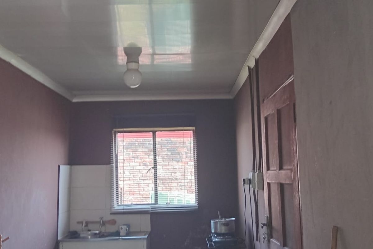 A basic, unfinished kitchen area featuring a sink, tiled splashback, and exposed wiring, offering significant potential for renovation and modernization.