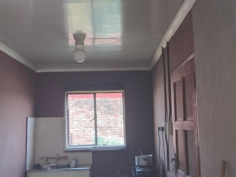 A basic, unfinished kitchen area featuring a sink, tiled splashback, and exposed wiring, offering significant potential for renovation and modernization.