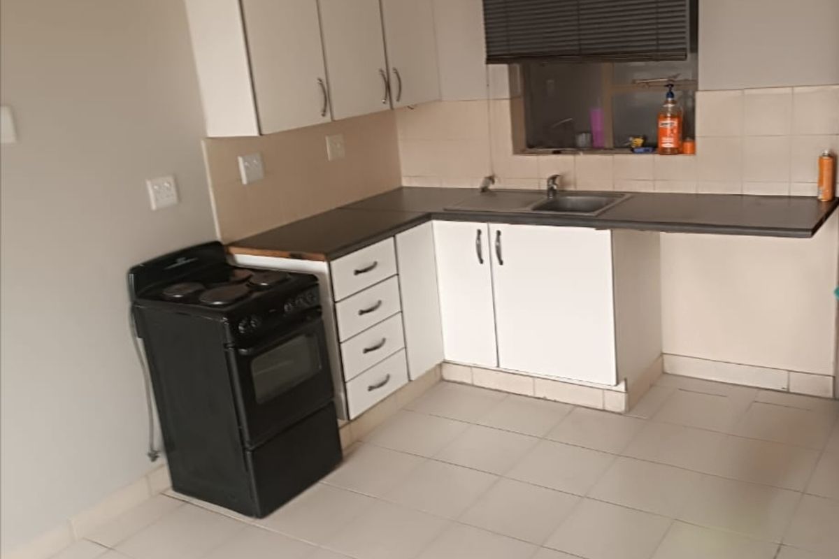 A functional kitchen featuring white cabinetry, tiled flooring, a stainless steel sink, and a tiled backsplash, offering a clean and practical workspace.