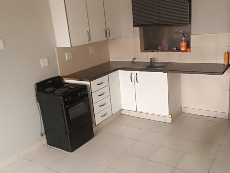 A functional kitchen featuring white cabinetry, tiled flooring, a stainless steel sink, and a tiled backsplash, offering a clean and practical workspace.