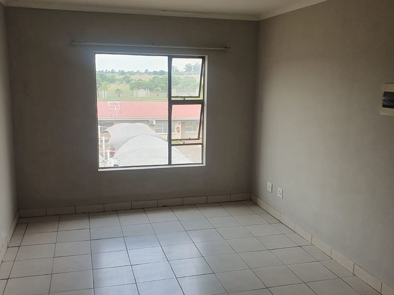 An empty bedroom featuring tiled flooring, neutral walls, and a window with natural light, providing a blank canvas for personalization.