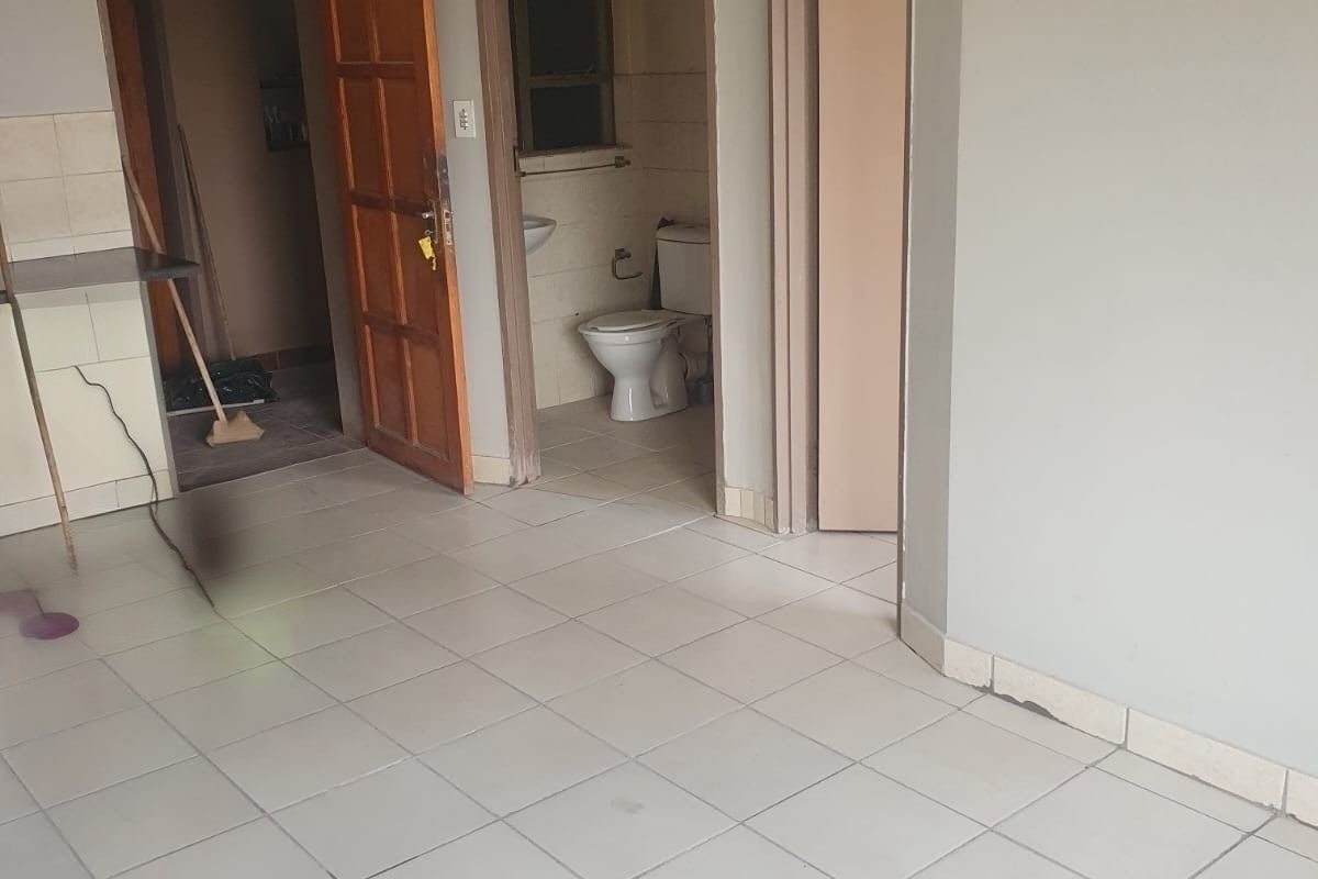An empty living area featuring ceramic tiled flooring, leading to a bathroom and additional room, requiring cosmetic updates to improve its overall condition.