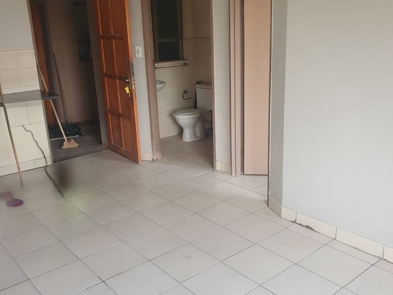 An empty living area featuring ceramic tiled flooring, leading to a bathroom and additional room, requiring cosmetic updates to improve its overall condition.