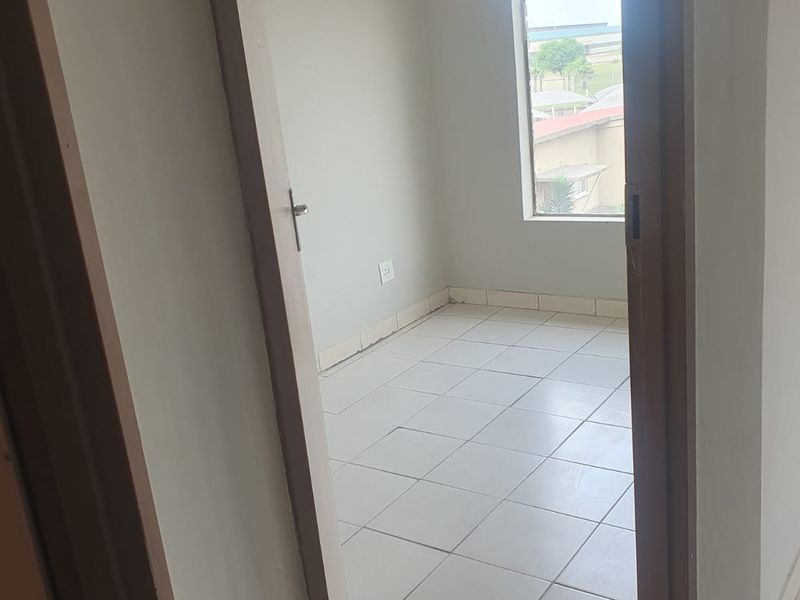 A vacant bedroom featuring neutral tiled flooring and a window providing natural light, ready for personalization.