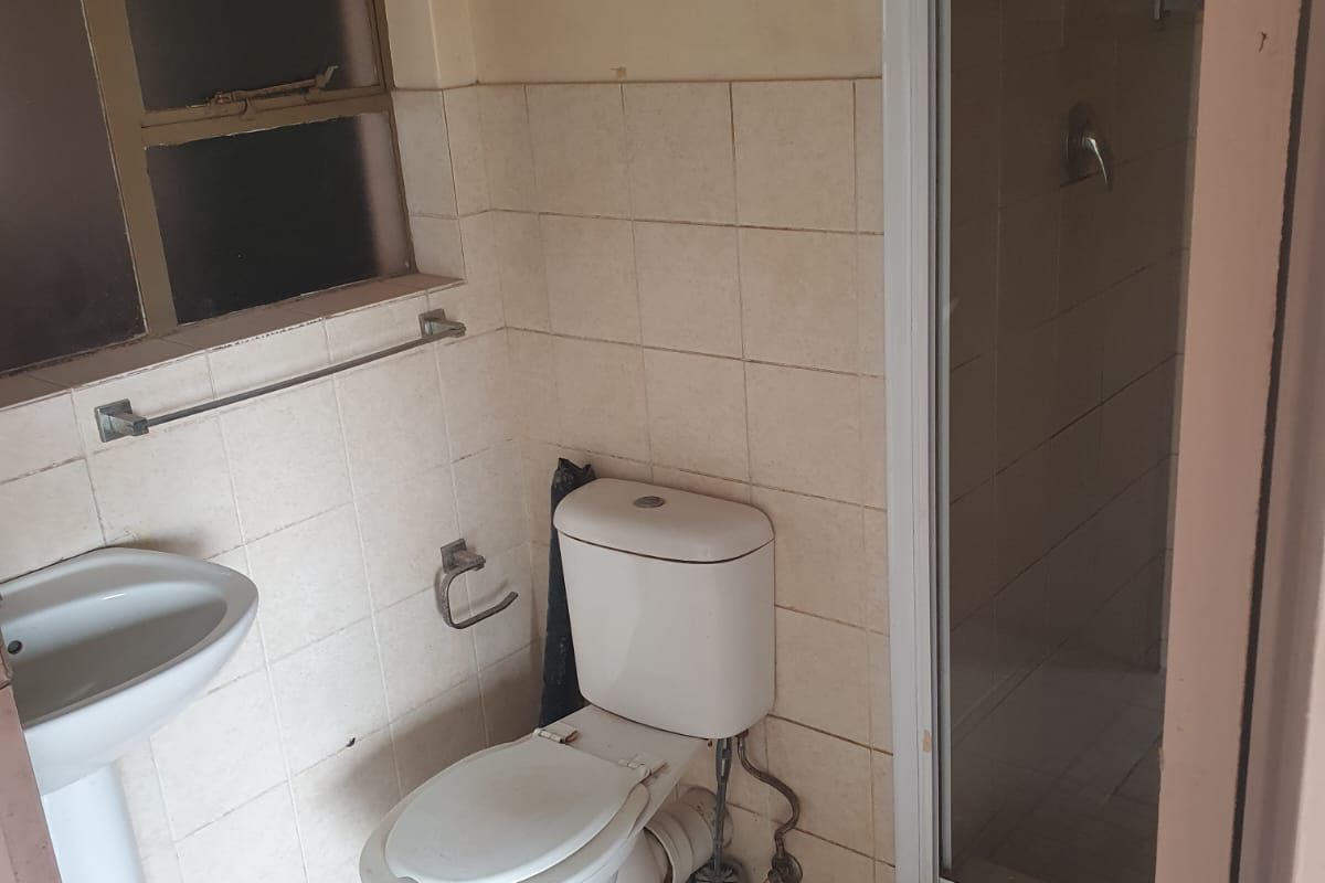 A functional bathroom featuring a pedestal basin, toilet, and a shower enclosure with tiled walls and flooring, requiring cosmetic updates.