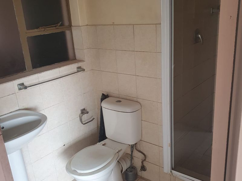 A functional bathroom featuring a pedestal basin, toilet, and a shower enclosure with tiled walls and flooring, requiring cosmetic updates.