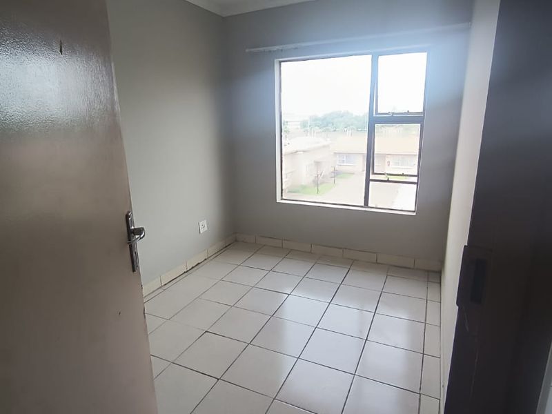 A vacant bedroom featuring neutral wall paint, tiled flooring, and a large window providing natural light.