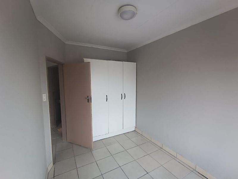 A clean, empty bedroom featuring neutral grey walls, tiled flooring, and a built-in white wardrobe.