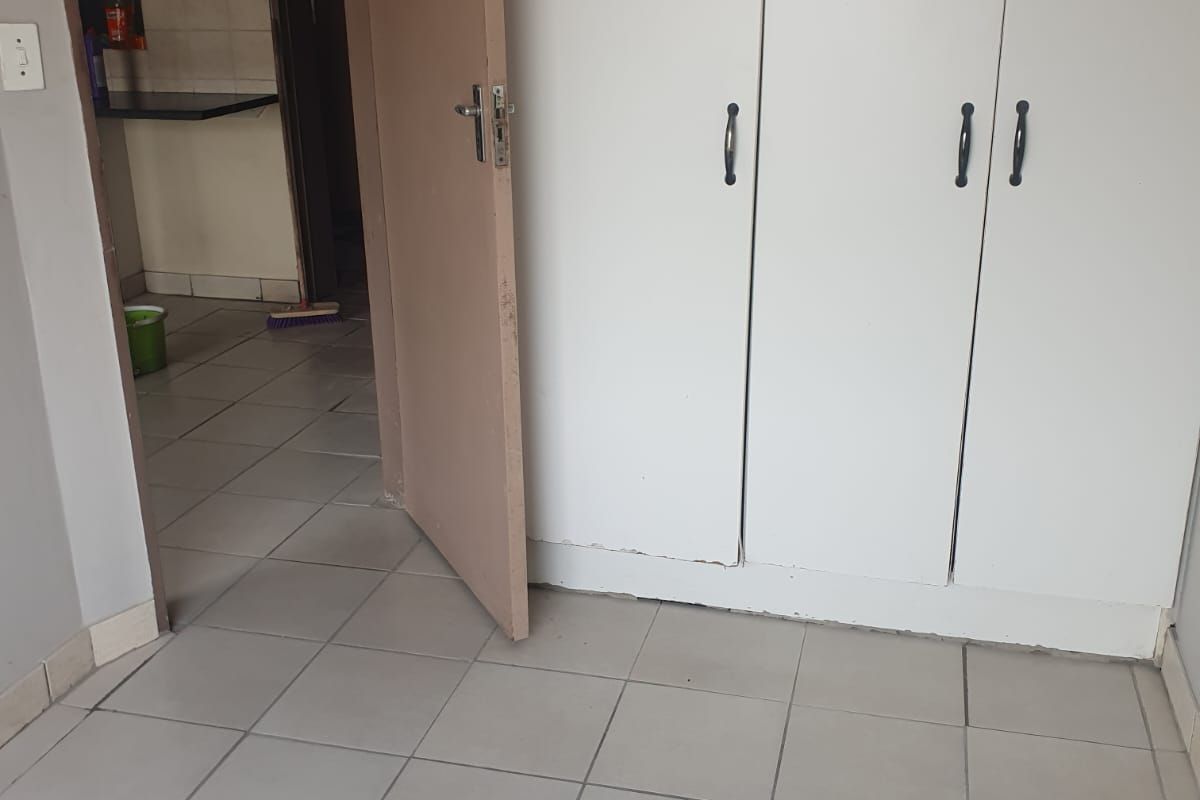 An empty bedroom featuring tiled flooring and built-in cupboards, with a view into the adjacent kitchen area.