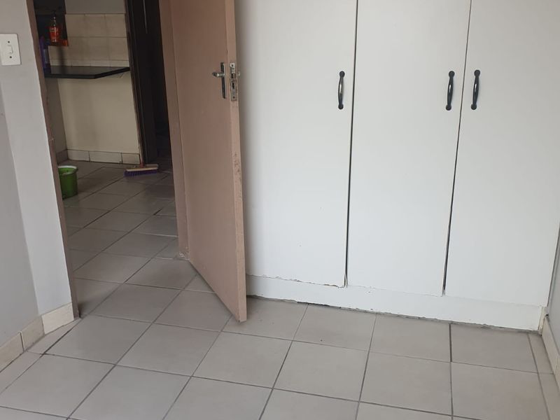 An empty bedroom featuring tiled flooring and built-in cupboards, with a view into the adjacent kitchen area.