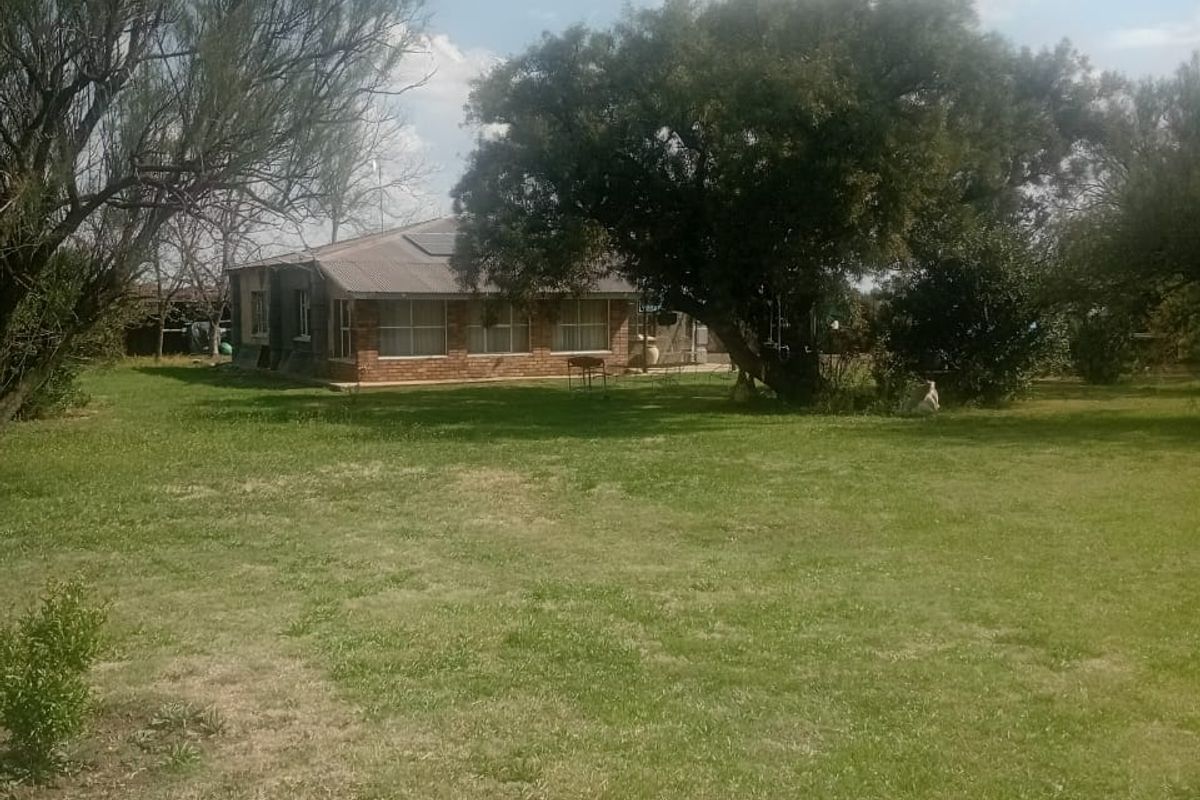 A view of the rear of the residential property featuring a brick exterior, metal roof, and a spacious surrounding lawn with mature trees.