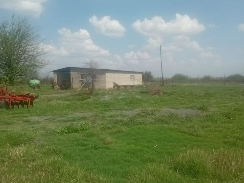 A view of a vacant residential land plot featuring an existing outbuilding structure, open grassy terrain, and perimeter fencing.