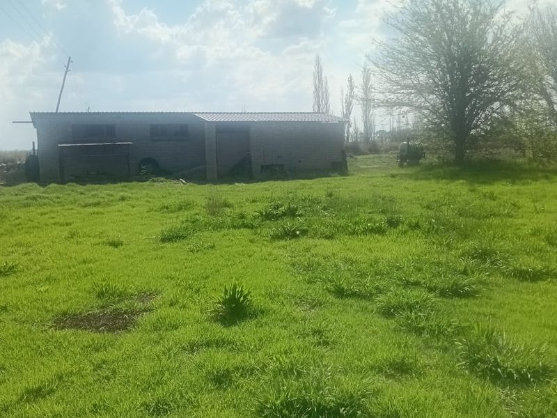 A view of a vacant residential plot featuring a small brick outbuilding set within an open, grassy landscape.