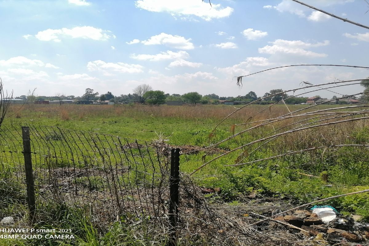 A view of a vacant residential plot featuring overgrown grass and damaged wire mesh perimeter fencing.
