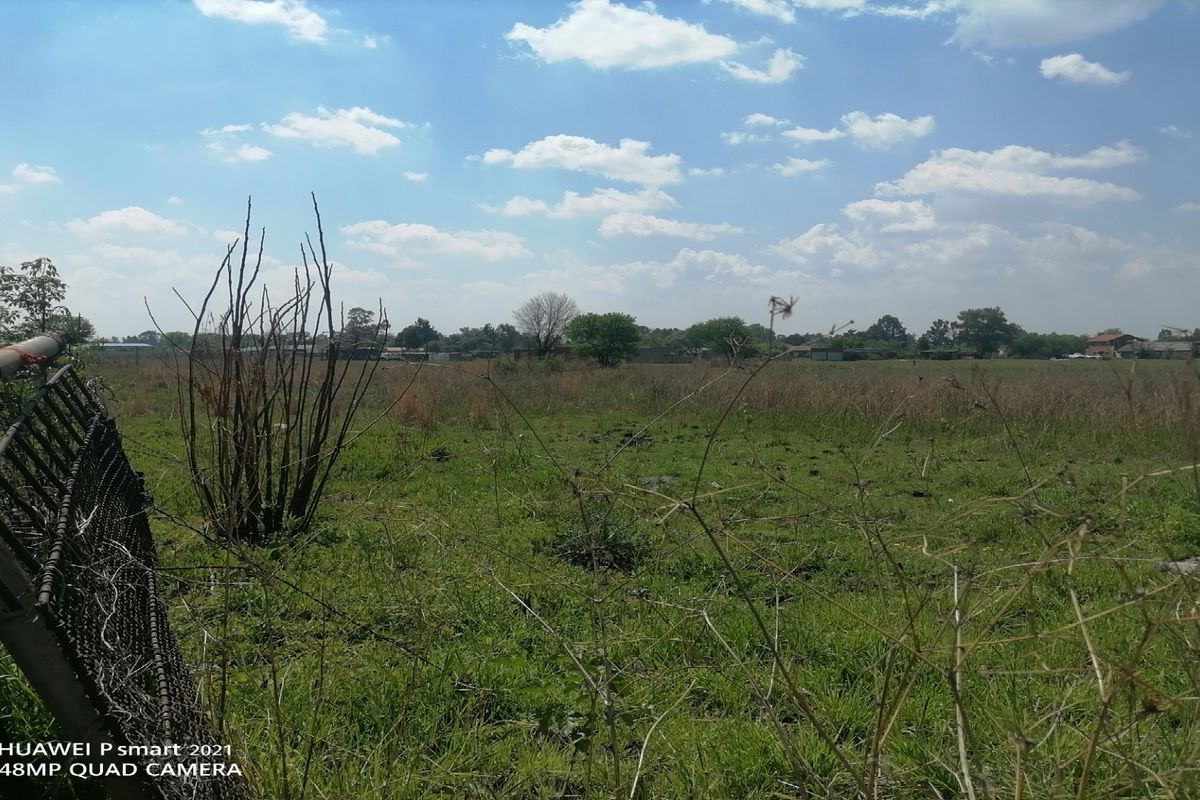 A view of a vacant residential plot featuring overgrown grass and damaged wire mesh perimeter fencing.