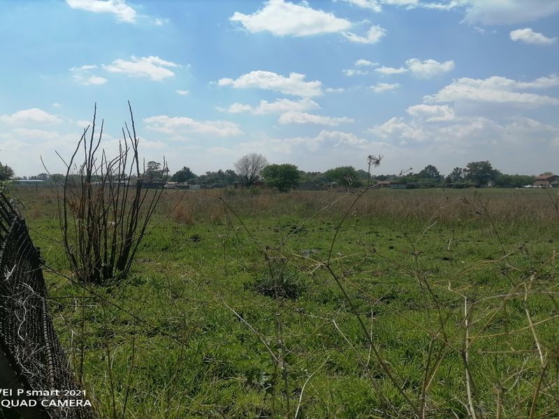 A view of a vacant residential plot featuring overgrown grass and damaged wire mesh perimeter fencing.