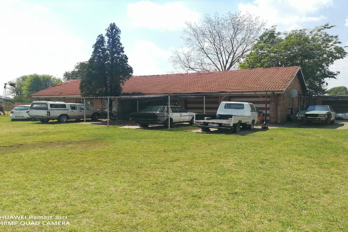 Rear view of a residential property featuring a brick facade, terracotta tiled roof, and an attached carport structure set on a large grassed lot.