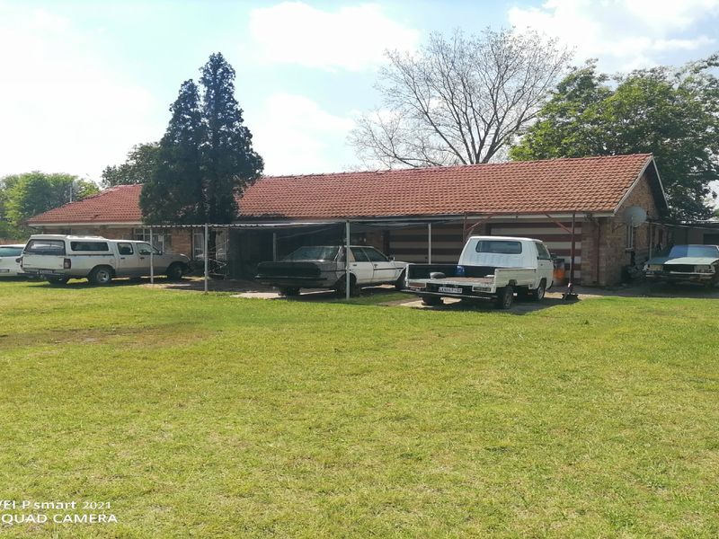 Rear view of a residential property featuring a brick facade, terracotta tiled roof, and an attached carport structure set on a large grassed lot.