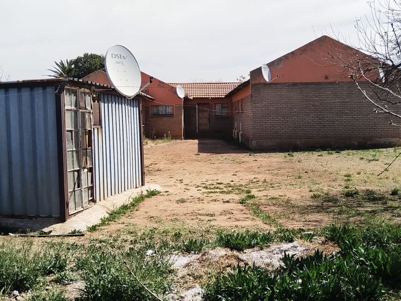Rear view of the property showing a brick house, a corrugated metal outbuilding, and an unpaved yard area.