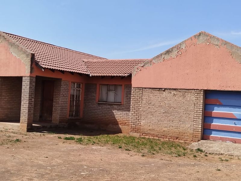 Front view of a single-story brick house featuring a tiled roof, covered entrance, and an integrated garage with a large dirt yard.