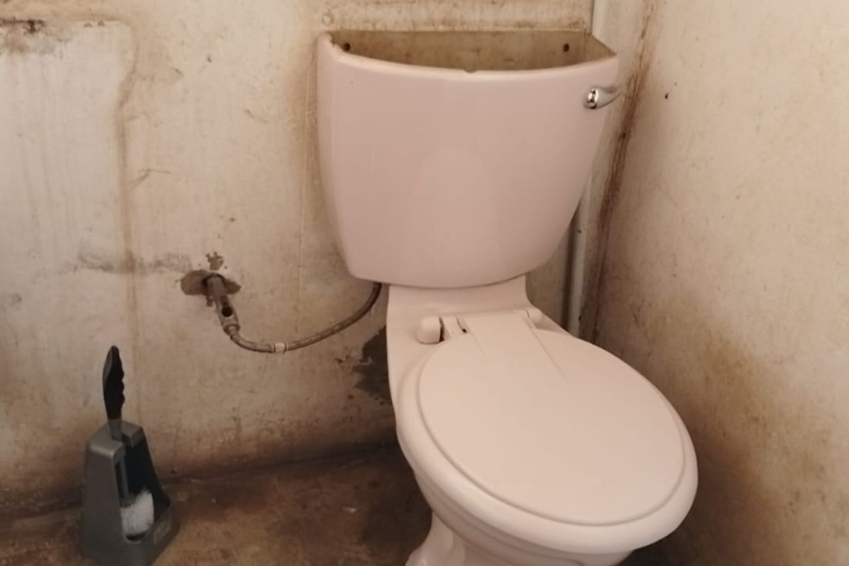 A bathroom in poor condition featuring a toilet with a missing cistern lid and significant wall staining requiring renovation.