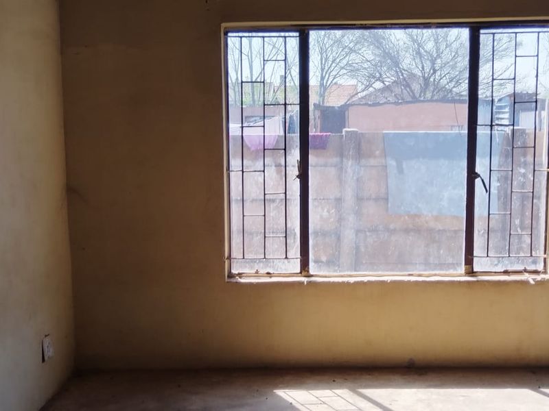 A vacant bedroom featuring a large window with security bars, requiring cosmetic updates to the wall finishes.