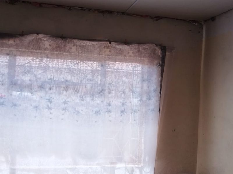 A bedroom interior showing significant wear to the walls and ceiling, featuring a window with security bars.