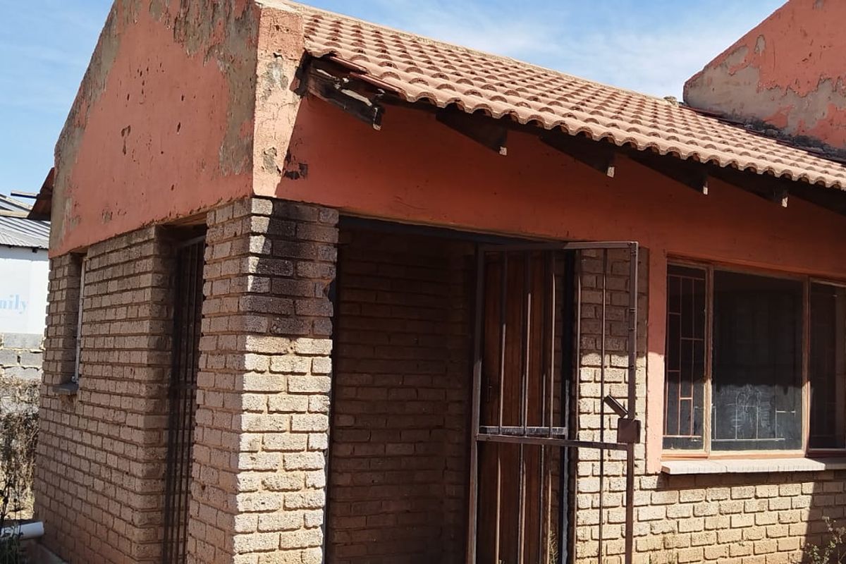 Rear exterior view of a brick house showing significant wear to the painted facade and roof eaves.