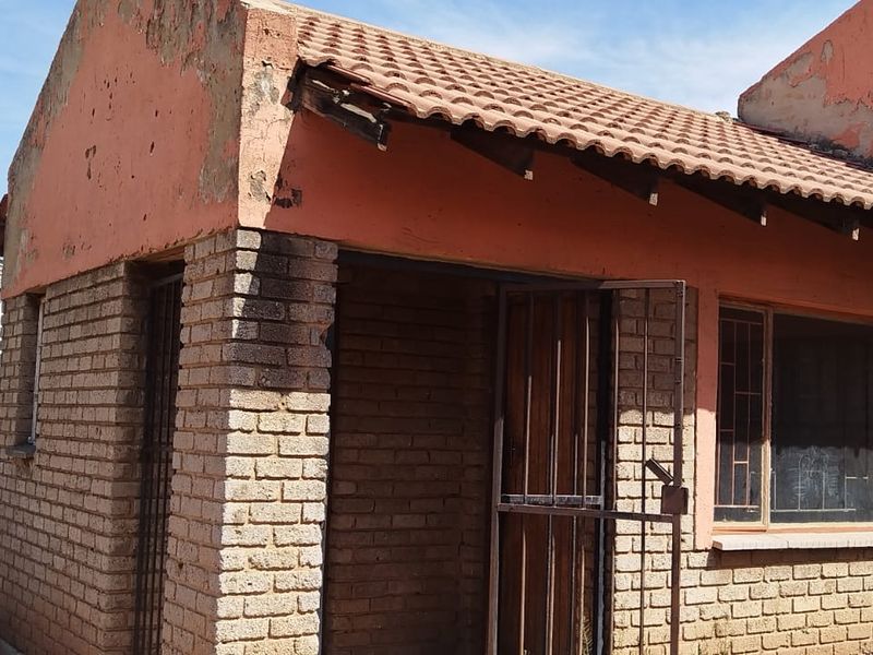 Rear exterior view of a brick house showing significant wear to the painted facade and roof eaves.