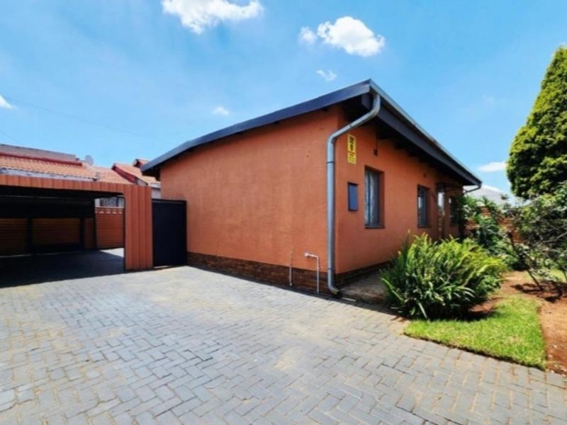 A well-maintained front exterior view featuring a paved driveway, a covered carport, and a neat garden area.
