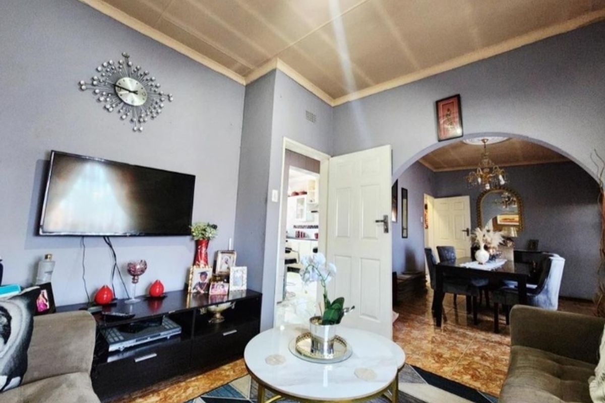 A living room featuring tiled flooring, a coved ceiling, and an arched entryway leading to the dining area.