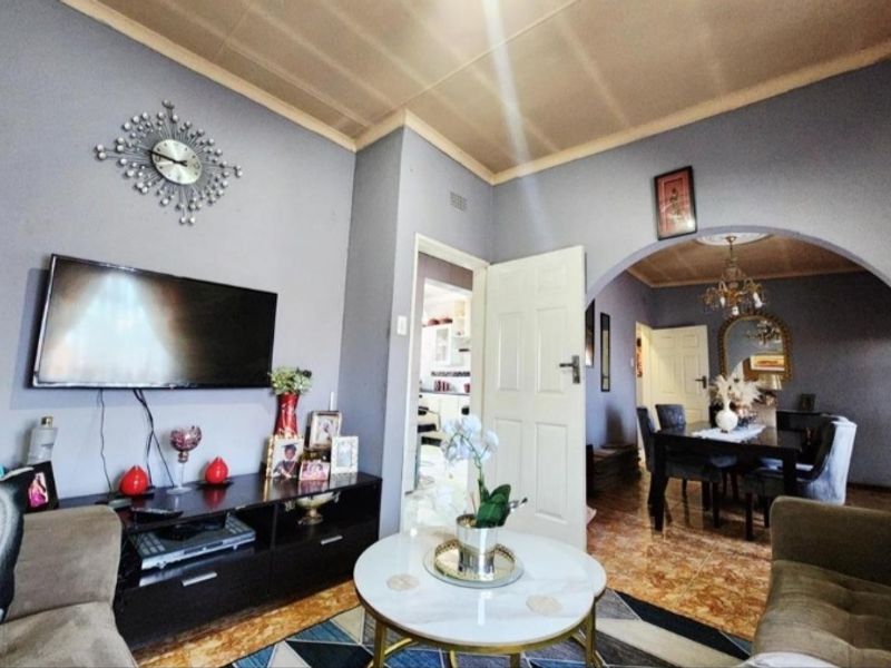A living room featuring tiled flooring, a coved ceiling, and an arched entryway leading to the dining area.