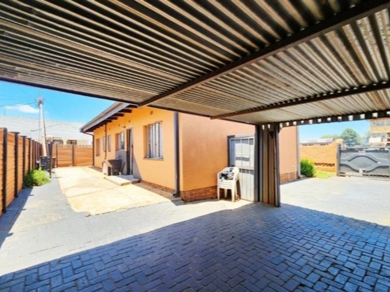 A covered carport area with corrugated metal roofing and paved driveway, providing secure off-street parking space.
