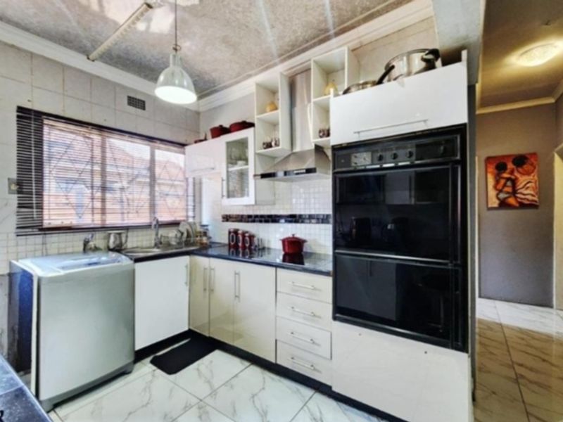 A functional kitchen featuring built-in cabinetry, a double oven, extractor fan, tiled backsplash, and marble-look floor tiles.